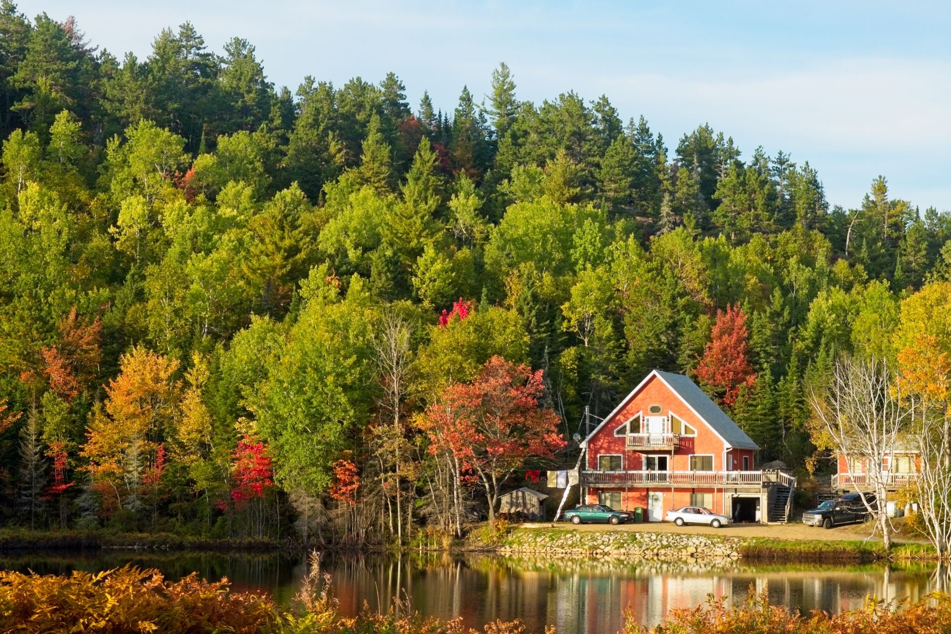 Idyllic lakeside cabin surrounded by vibrant autumn forest landscape.